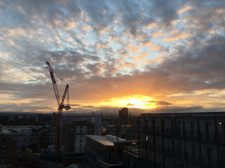Sunset over Manchester with cranes and buildings.